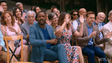 a group of people sitting in chairs applauding with a netflix logo on the bottom right