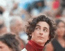 a young man with curly hair is wearing a red turtleneck and looking up .
