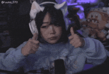 a girl wearing a cat ear headset is giving a thumbs up