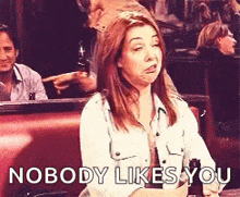 a woman is sitting at a table with a bottle of beer and the words nobody likes you .