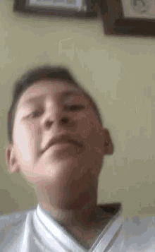 a young boy in a white shirt is making a funny face in front of a wall .