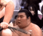 a sumo wrestler is being tied up with a rope while a crowd watches .