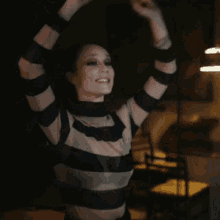 a woman in a striped shirt is raising her arms in the air and smiling