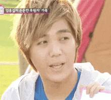 a young man with blonde hair and a blue shirt is holding a piece of paper .