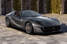 a gray ferrari is parked in front of a building on a brick pavement .