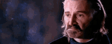a man with long hair and a beard is looking at the camera with a sad look on his face .