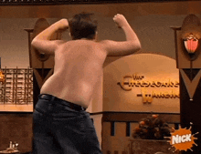 a shirtless man flexes his muscles in front of a sign that says cheesecake