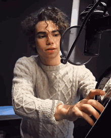 a young man in a white sweater is standing in front of a microphone