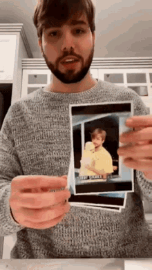 a man in a grey sweater is holding a picture of a boy in a yellow shirt .