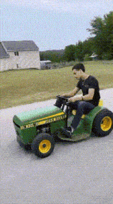 a man is riding a john deere lawn mower down the road