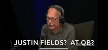 a man wearing headphones is sitting in front of a microphone and saying justin fields ? at qb ?