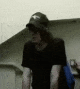a man wearing a black hat and sunglasses is standing in a room .