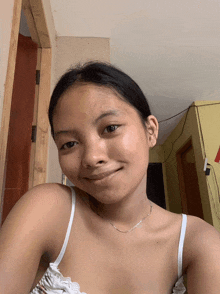 a young girl wearing a white tank top and a silver chain smiles for the camera
