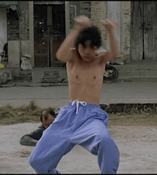 a shirtless man in blue pants is doing a karate move .