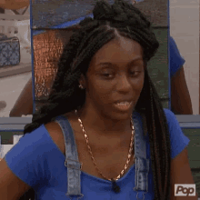 a woman wearing a blue shirt and overalls is looking at the camera .