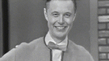 a man in a suit and bow tie is smiling in a black and white photo .