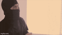 a person wearing a mask is sitting at a desk using a laptop computer .