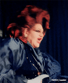 a drag queen with red hair is wearing a blue shirt and earrings
