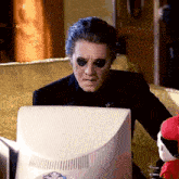 a man in a black suit is sitting in front of a computer screen .