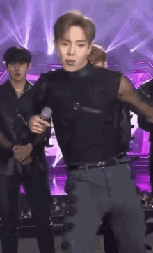 a man is holding a microphone while standing on a stage with other men .