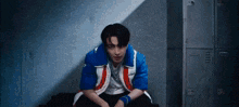 a man in a blue and red jacket is sitting in front of a locker .