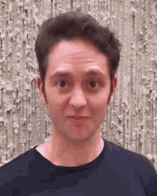 a man in a black shirt is making a funny face in front of a wall .