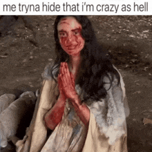 a woman with blood on her face is sitting on the ground with her hands folded in prayer