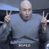 a bald man is making a peace sign with his hands while sitting in a chair .