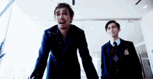two men are standing next to each other and one has a crest on his jacket that says ' umbrella academy '
