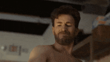 a shirtless man with a beard is standing in a room .