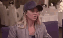 a woman wearing a baseball cap and a gray jacket is sitting at a table in a restaurant .