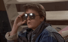 a man wearing sunglasses and a denim jacket looks at the camera