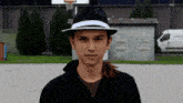 a young man wearing a fedora stands in front of a basketball net