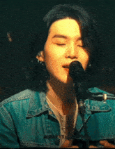 a young man with long hair is singing into a microphone while wearing a denim jacket .