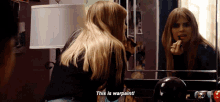 a woman applying lipstick in front of a mirror and says this is warpaint