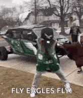 a man in a green eagles jersey is holding a baseball cap in front of a green vehicle .