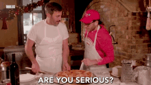 a man in a red hat says " are you serious " while another man prepares a pizza