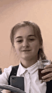 a girl is taking a selfie with her phone and holding a glass of soda
