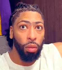 a man with a beard and braids is making a funny face while wearing a white shirt .