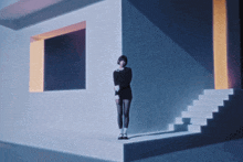 a woman in a black dress stands in front of a white wall and stairs