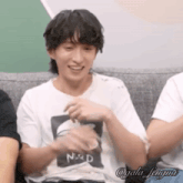 a man in a white t-shirt is sitting on a couch with his arms crossed and smiling .