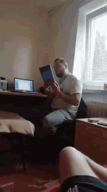 a man is reading a book while sitting at a desk in front of a laptop
