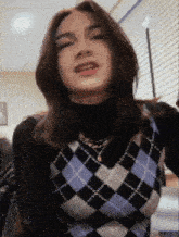 a young woman wearing a plaid vest and a black turtleneck is making a funny face .