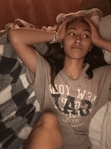 a girl laying on a bed with her hands on her head wearing a grey shirt that says ' new york ' on it
