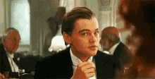 a man in a tuxedo is sitting at a table in a restaurant with a glass of wine in his hand .