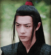 a young man with long black hair has a red ponytail