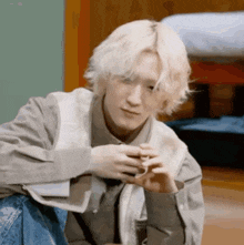 a young man with blonde hair is sitting on the floor looking at something