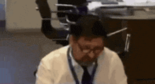a man in a white shirt and tie is sitting at a desk in an office .