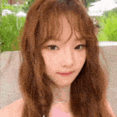 a close up of a woman 's face with long brown hair and a pink necklace .