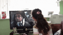 a woman is watching a tv show with a man in a suit on it